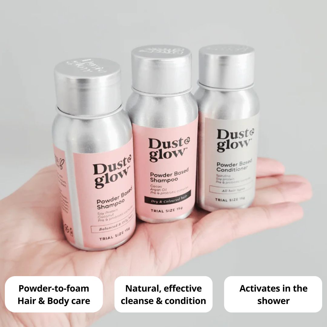 Hand holding three trial-size bottles of Dust & Glow powder-based hair care products.