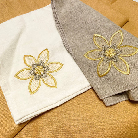 Servetter av tyg: linne och halvlinne med broderade blommor på dov gul bakgrund.