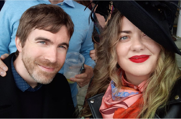 A silk scarf designer and artist from Ireland at the Galway Races wearing a peach luxury silk scarf with boyfriend watching horse racing