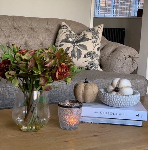 autumnal coffee table decor including a glass vase with autumn faux flowers and decorative pumpkins and candle light