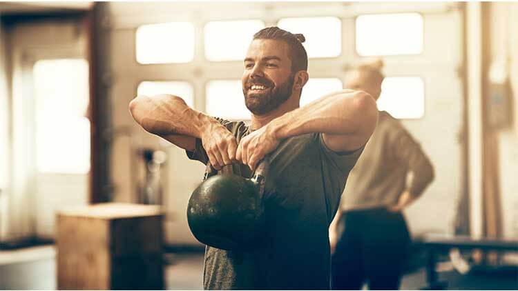 Fit young man smiling while lifting dumbbells in a gym