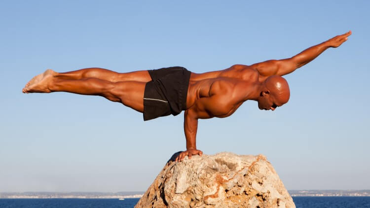 Man using one hand to balance on rock in front of ocean