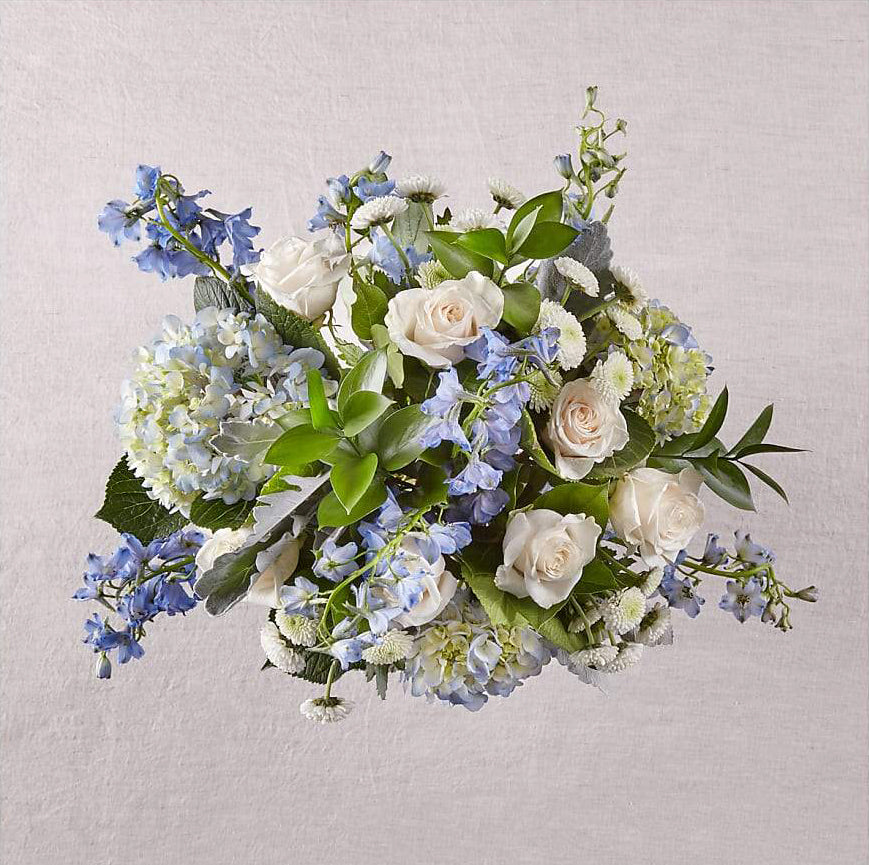 Blue and white floral arrangement designed with premium hydrangea, delphinium, roses, mums and foliage.