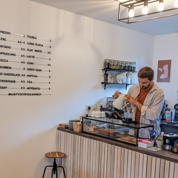 The interior of Hiatus Coffee in Annency. The owner is pouring a filter coffee behind the bar.