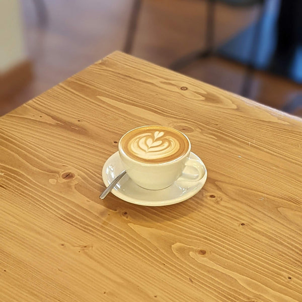 A milk coffee with nice latte art on a saucer, atop a wooden table.