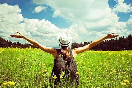 Image of a woman hiking in a field of wildflowers throwing her arms wide in wonder