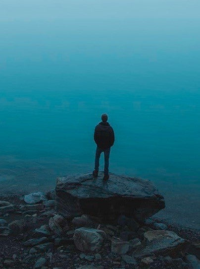 Image of a man standing alone facing a vast sea