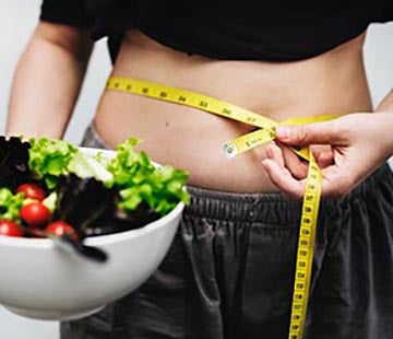 image of woman measuring her waist and eating a salad