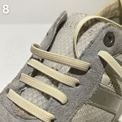 Instructieve close-up van beige veters rijgen in een grijze schoen met een strak straight-bar patroon