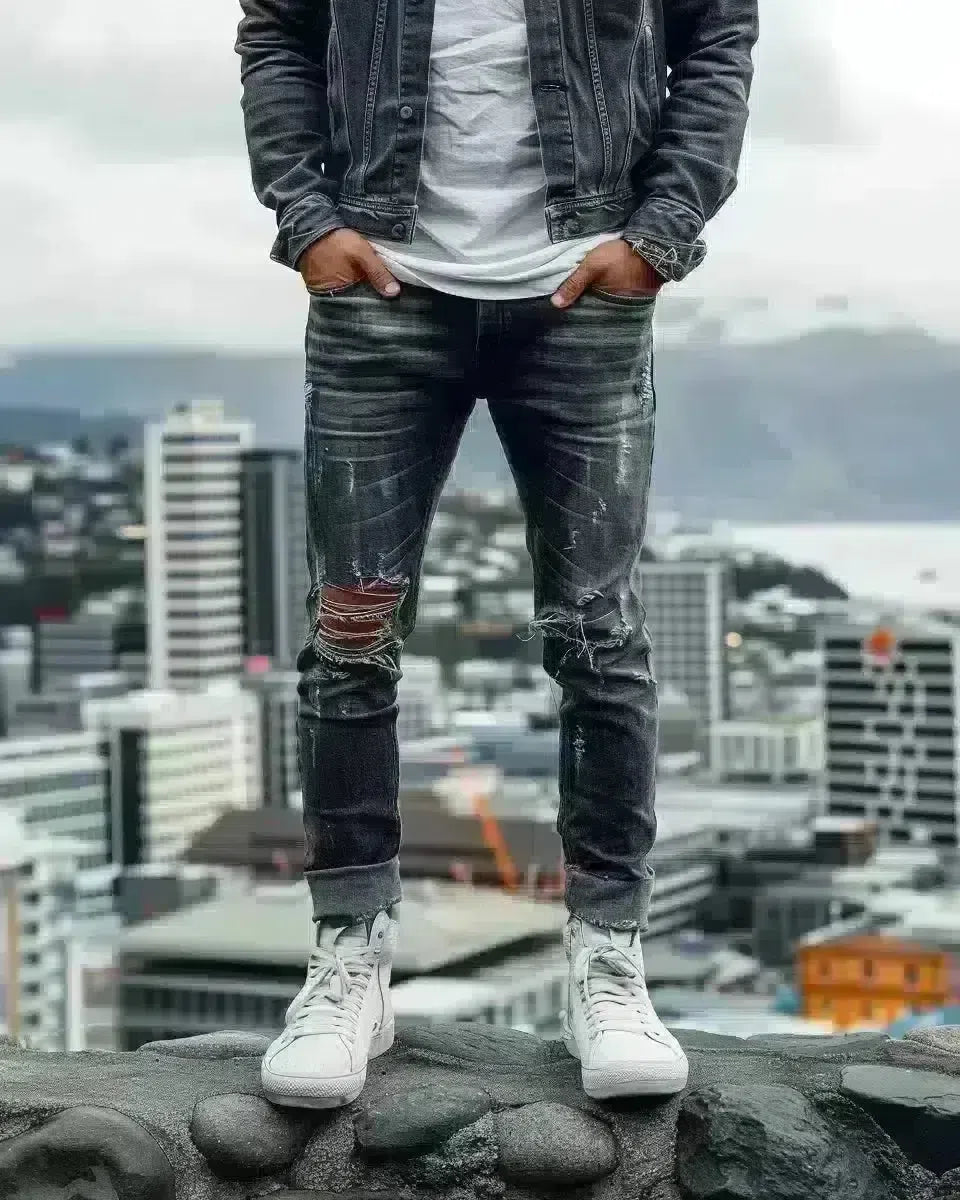 Man in ripped black jeans, Wellington cityscape backdrop, denim detailed. Spring season.