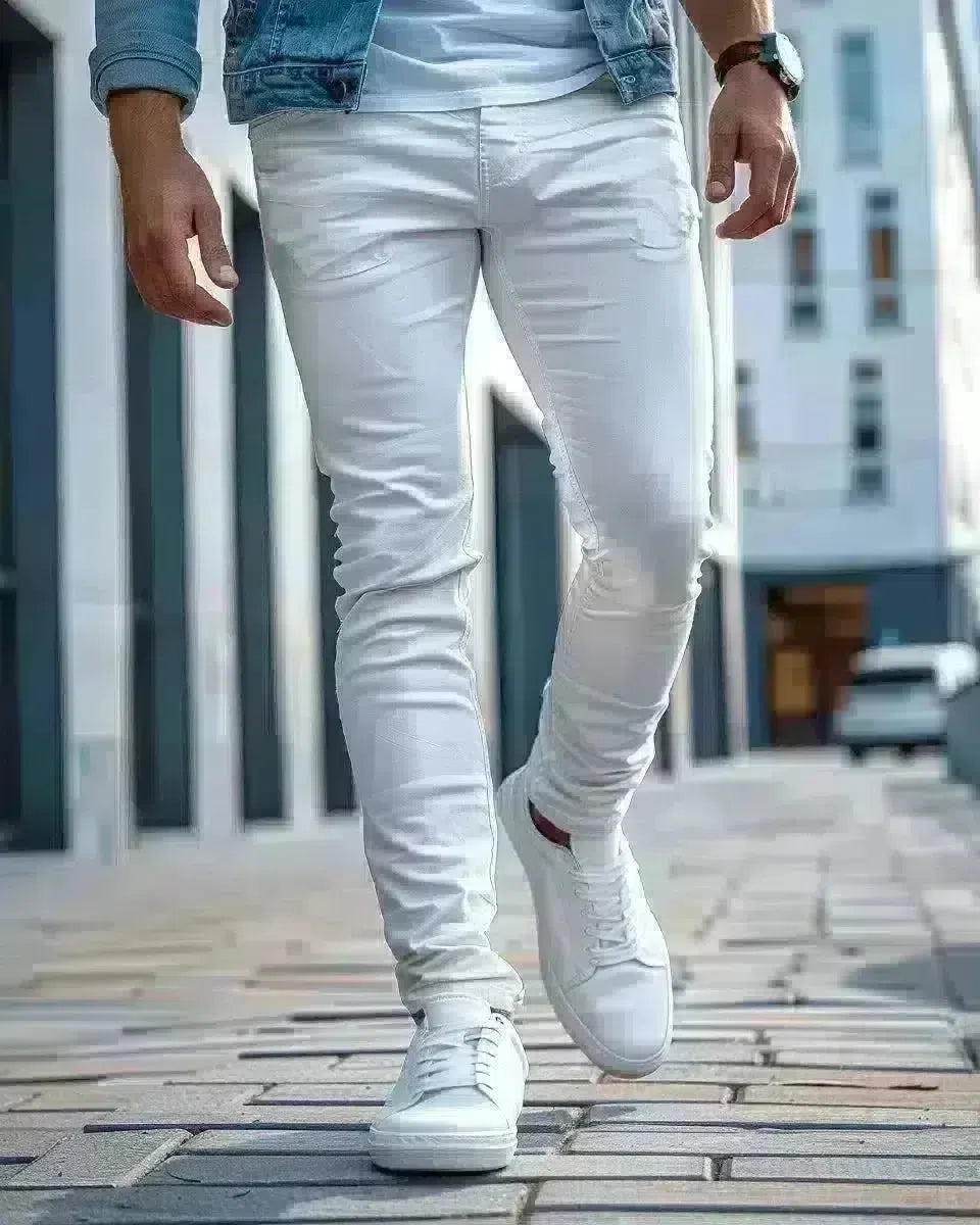 Olive-skinned man in slim-fit white jeans, outdoor urban background, denim detail. Spring season.