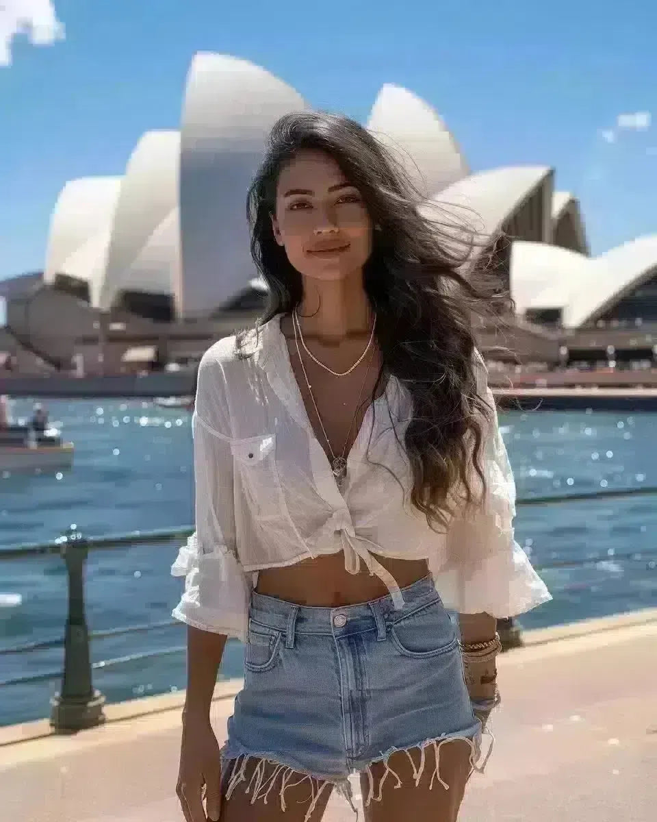 South Asian woman in high waisted denim shorts, white blouse at Sydney Opera House. Spring season.