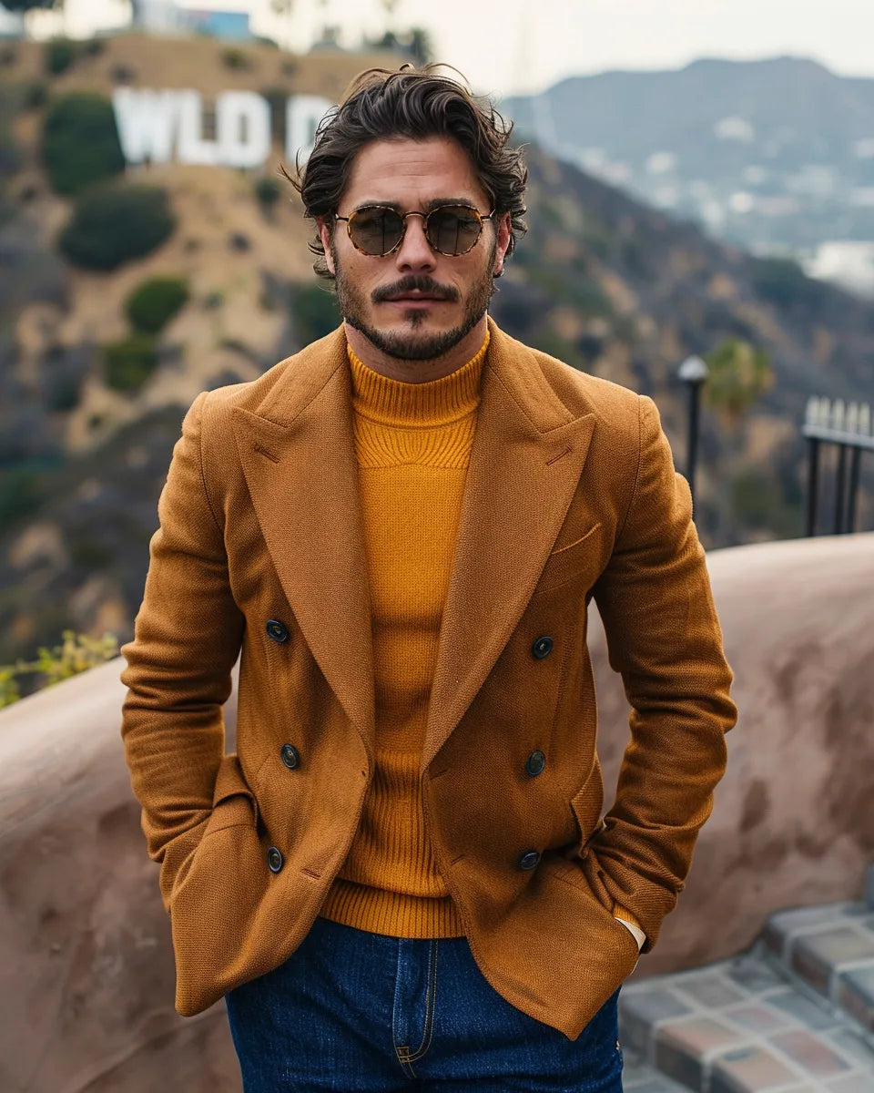 Man in deep indigo high-waisted jeans, mustard yellow chunky sweater, and burnt orange blazer. Fall tones. Summer season. Latino male. Hollywood Sign, Los Angeles, CA city background.