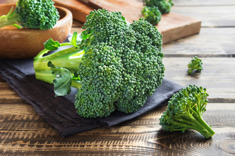 raw broccoli crown with stem lying on wooden table