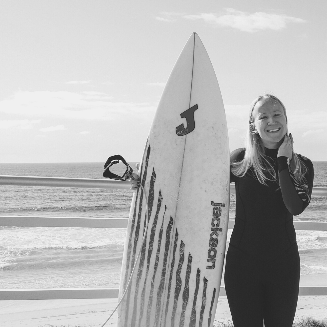 Black and white photo of a girl with a surfboard with ocean at the background.