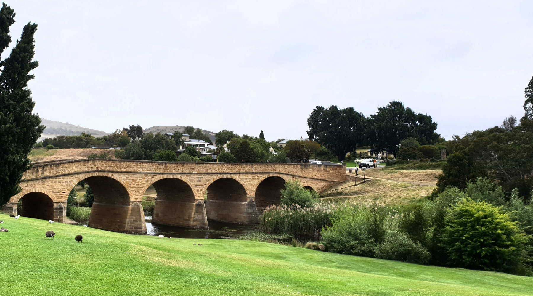 An old brick bridge across a river with lush green riverbanks.
