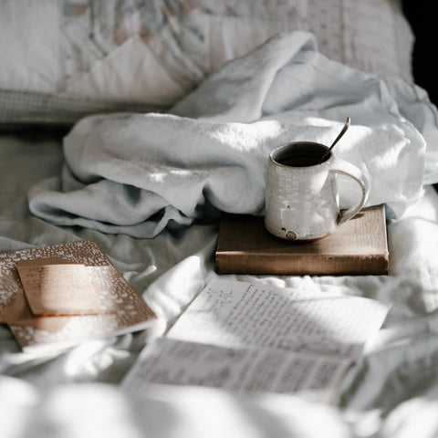 tasse de café et un livre sur un lit avec des draps blancs.