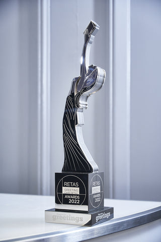 Image of a Reta Award which is a woman reaching her hands up looking at a greetings card she has in her hands.