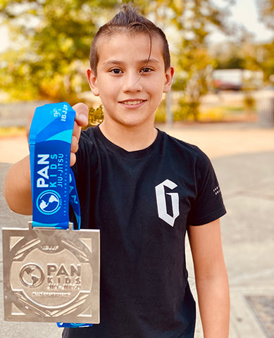 Hank holding Pans medal while wearing Gameness BJJ shirt.