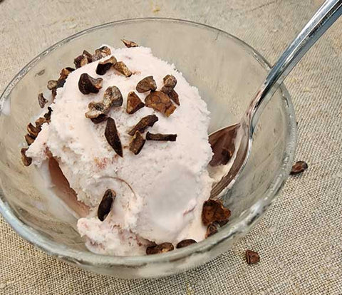 cacao nibs sprinkled on strawberry ice cream in a glass bowl