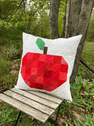 Scrappy Apple quilt block pattern by Penny Spool Quilts - pillow outdoors on a chair featuring red scrappy apple with brown stem and green leaf
