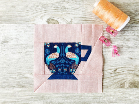 Teacup FPP Quilt Block Pattern by Penny Spool Quilts - blue teacup with fussy-cut peacock fabric on pink textured background