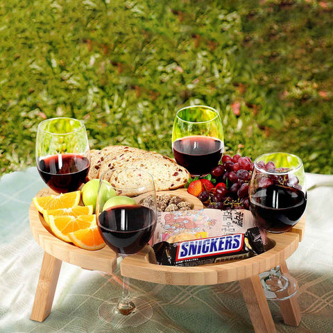 Picnic table with wine and lots of snacks, outdoors.