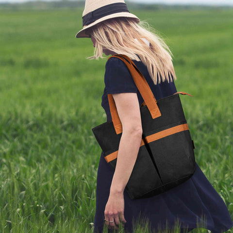A girl in a black dress on the grass with her backpack blowing in the wind