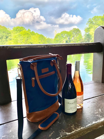 Two bottles of red wine next to the wine bag, surrounded by a nice blue sky and green mountains