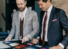 Two men in well made suits reviewing suit fabric swatches