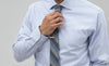 Blue button down shirt with a tri-color striped tie and a silver tie bar