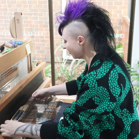 goth girl with mohawk weaving on a floor loom
