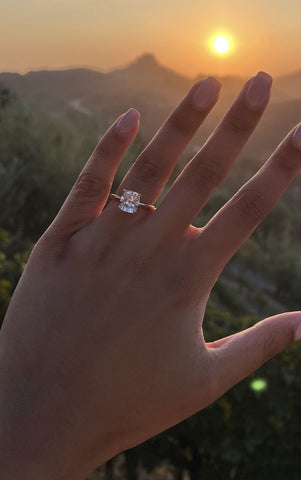 Hand silhouetted against a sunset, revealing a diamond engagement ring.