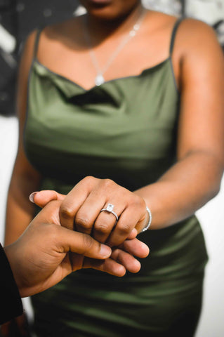 An affectionate moment captured as a man gently holds his girlfriend's hand, showcasing the beautiful engagement ring. The ring gleams with a brilliant diamond, symbolizing their love and commitment.