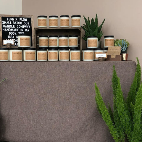 Closeup photo of Fern x Flow's soy candle display featuring handmade, 100% soy candles surrounded by various succulents and a large, green fern,