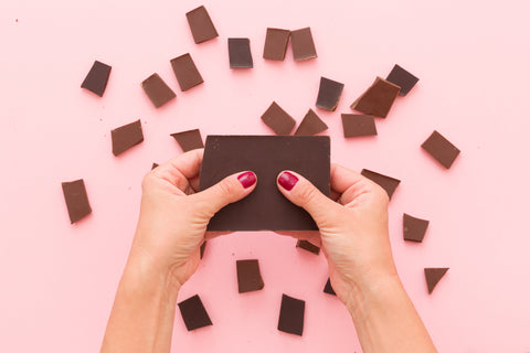 Girl with pink nails breaking dark chocolate over a pink background