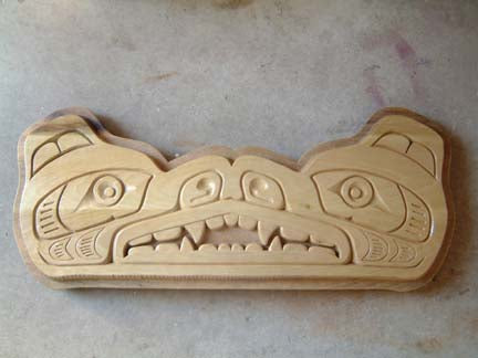 Native American bear art style, wood bear carving in Pacific Northwest Coast Native art style where profiled bear heads are facing each other and joined at the nose, mouth, teeth, and lips resulting in a face-on design of the bear.