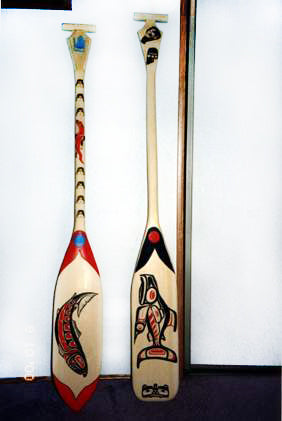 Two canoe paddles with Pacific Northwest Native American salmon art style designs painted in red, black, and blue. 