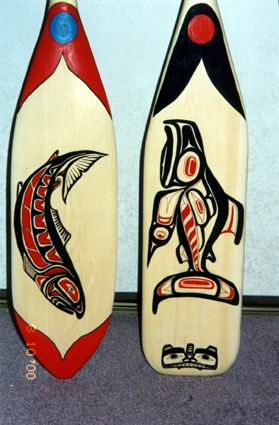 Two canoe paddles with Pacific Northwest Native American salmon art style designs painted in red, black, and blue. 