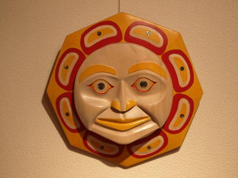 Pacific Northwest Native American sun art style wood carving with circle sun face and ovoids as sun rays, painted yellow, red, and orange. 