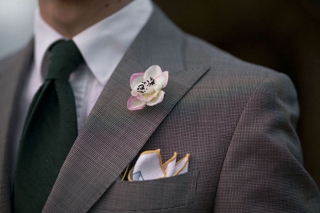 Das Einstecktuch in der Brusttasche und die seidene Boutonnière im Knopfloch des Jacketts