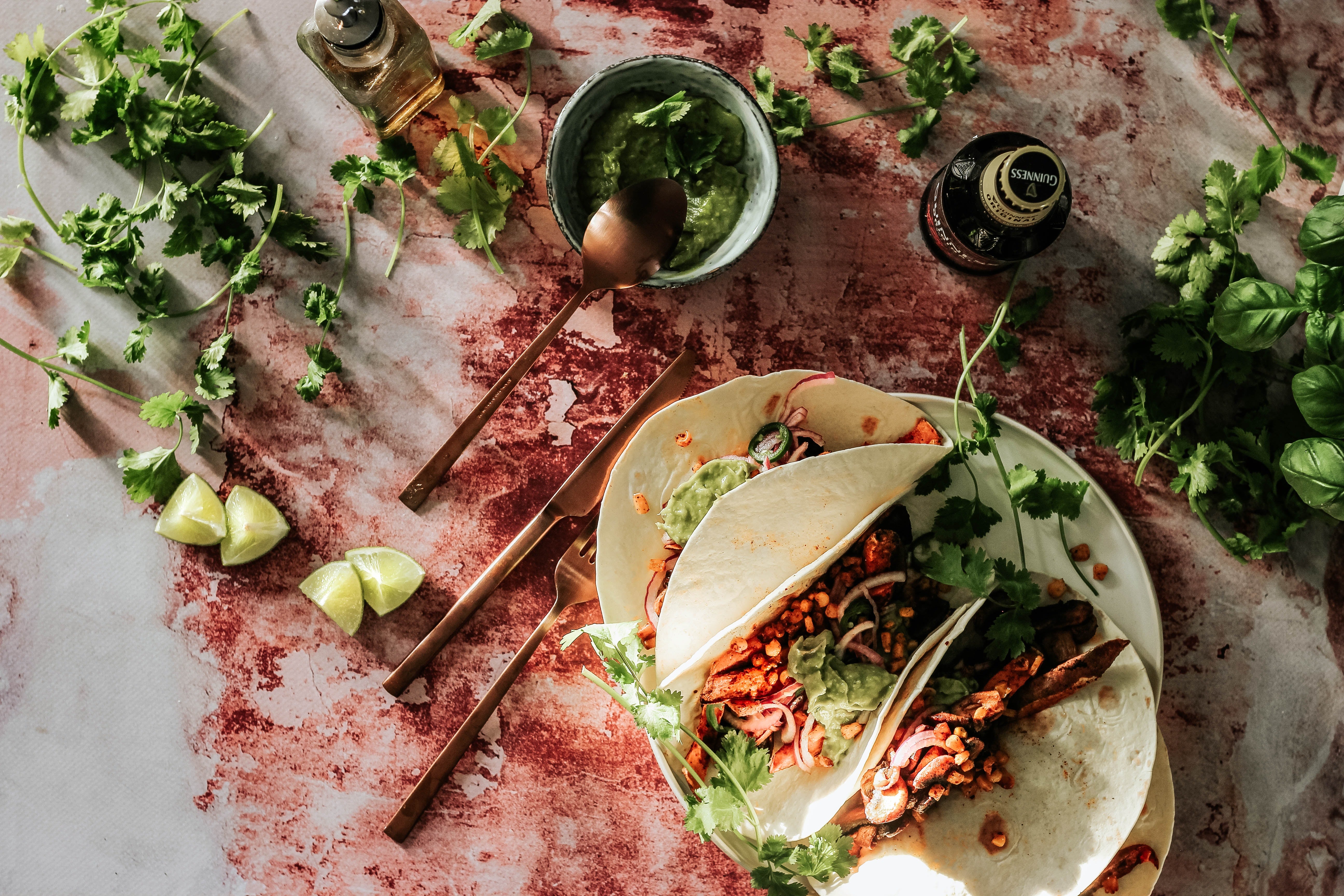 Chicken Cutlet Fajitas sitting on a table that has red and white splotches surrounded by cilantro basil and a bowl of guacamole.