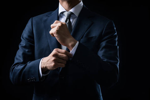 Man adjusting his sleeve beneath a dark suit blazer