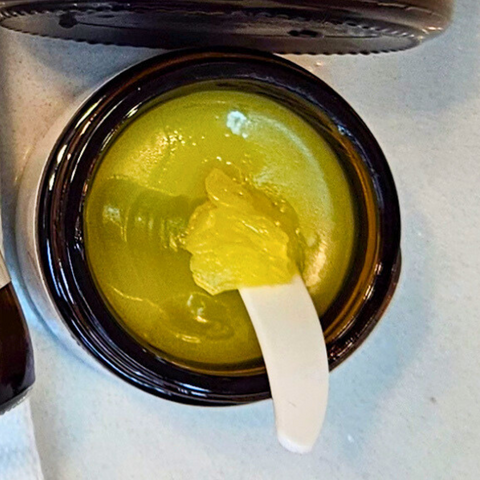 Jar of Eczema Salve with a beauty spatula, showing its creamy texture