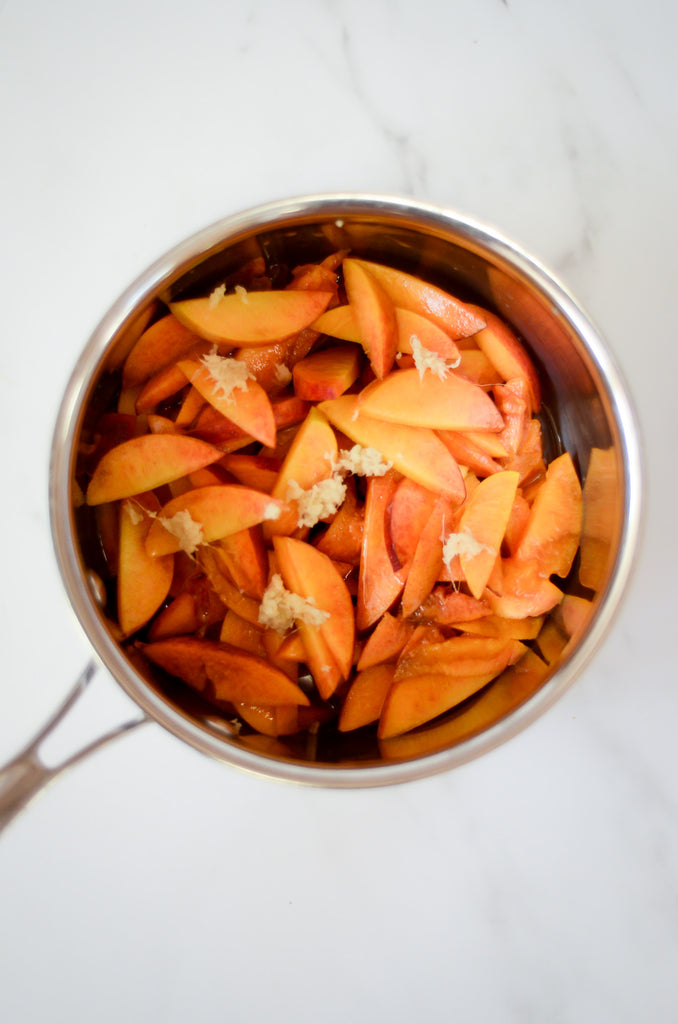 Photo of sliced fresh peaches with bits of fresh ginger in a pot to cook