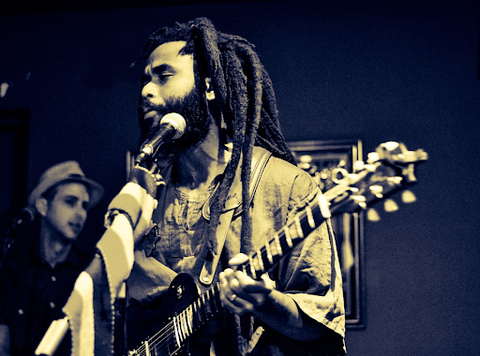 A musician with congo locs performing for a crowd.