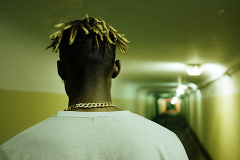 A view of the back of the head of a black man with short blond dreadlocks walking in a tunnel.