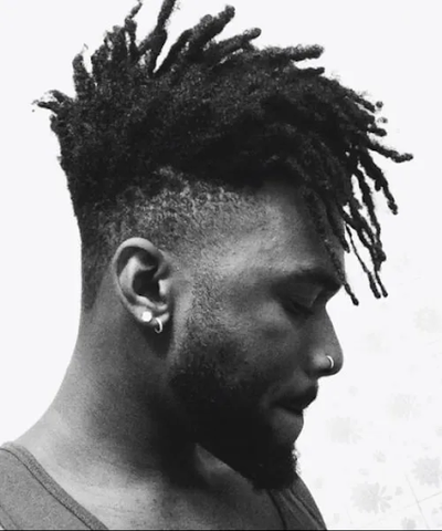 Side profile of a man with a rugged, dreadlock mohawk with a long front. 