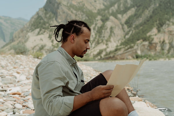 a man with dreadlocks reading a book outside 