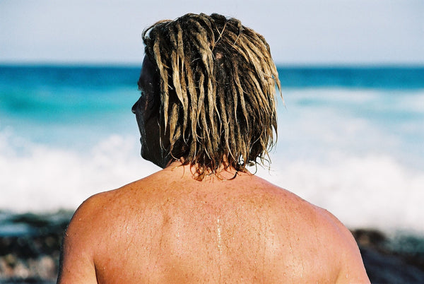 A man with blonde dreadlocks staring at the beach